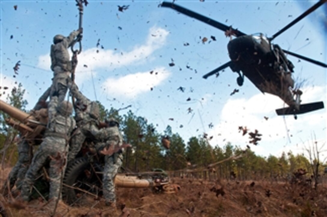 Leaves and twigs are whipped into the air by the rotor wash of UH-60 Black Hawk helicopter as soldiers prepare to hook up an M119A2 105mm howitzer during air assault training at Fort Bragg, N.C., on Feb. 8, 2013.  The soldiers are assigned to 3rd Battalion, 319th Airborne Field Artillery Regiment.  