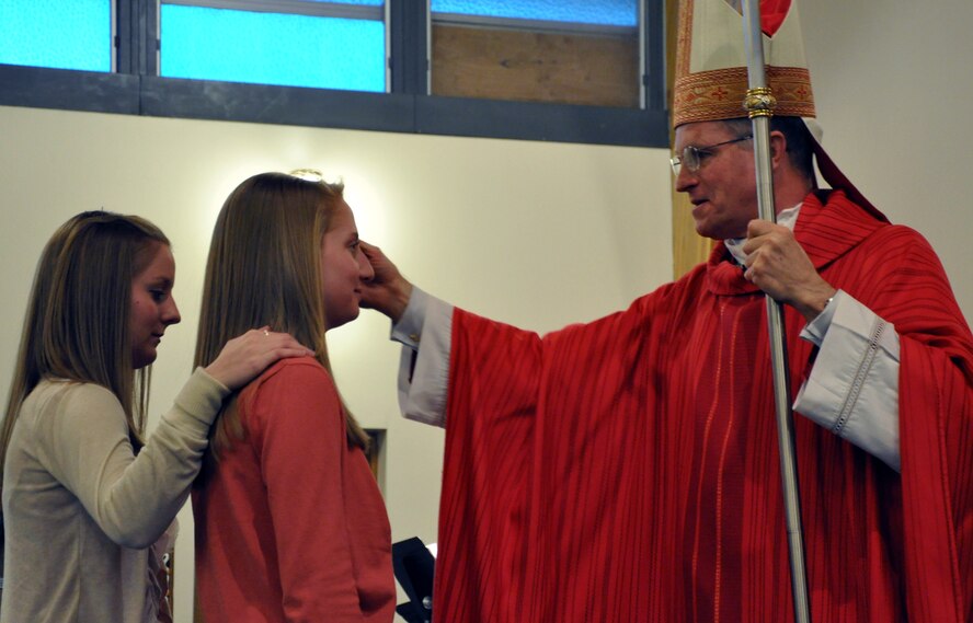 Archbishop Timothy Broglio, Archbishop of Military Services, confirms Mariah Klawon, as her sister, Haley, stands as her sponsor during confirmation Mass Feb. 7 at the High Plains Chapel. (U.S. Air Force photo by Senior Airman Dan Gage)