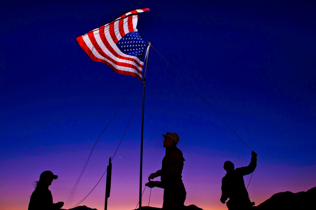 Service members raise a flag at the main camp during Fleet Combat Camera Pacific's Winter Quick Shot 2013 field training exercise at Burro Canyon Shooting Park in Azusa, Calif., Feb. 11, 2013. Quick Shot is a semi-annual exercise that improves combat camera service members' ability to operate in a combat environment. 