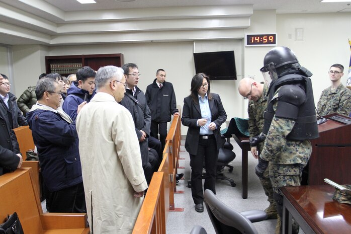 Master Sgt. Wade Campbell, pre-trial facilities officer-in-charge, and Lance Cpl. Kyrien Clark, corrections specialist, demonstrate padded equipment used to subdue hostile defendants awaiting trial in the pre-trial facility of the Station Judge Advocates courtroom here, Feb. 7, 2013, during an outreach program offered to Hatsukaichi police inspectors. The inspectors received many briefs in regards to standard operating procedures of military personnel stationed in Iwakuni.