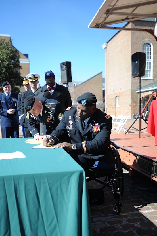 Army Col. Gregory D. Gadson, garrison commander, Fort Belvoir; and Army Sgt. Maj. Chester D. Grelock, garrison command sergeant major, Fort Belvoir; sign the fifth annual Armed Forces Community Covenant signing at Market Square in Alexandria on Monday. Representatives from Marine Corps Base Quantico, Fort Belvoir, the Military District of Washington, the Naval Support Activity, local leaders and the public attended to support the community and military.
