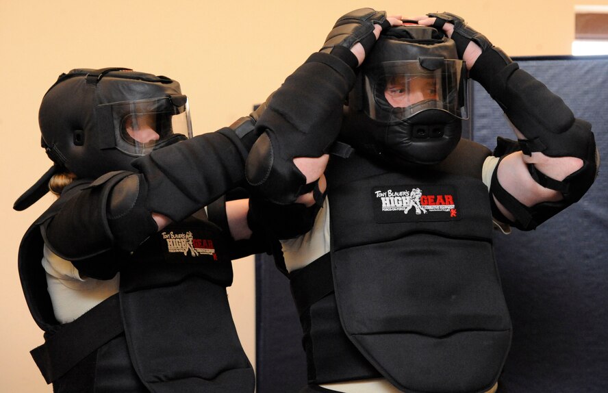 Tech. Sgt. Heather Geer, 2nd Security Forces Squadron unit training instructor, assists Tech. Sgt. William Townsend, 2 SFS unit training instructor, don his protective gear prior to beginning the application of force section of expandable baton training on Barksdale Air Force Base, La., Feb. 15. After instructing the students in techniques and procedures, Geer and Townsend played out various scenarios using the strikes taught. (U.S. Air Force photo/Airman 1st Class Andrew Moua)