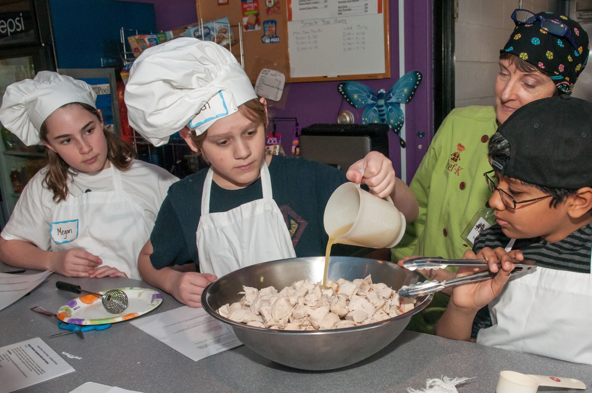 HANSCOM AIR FORCE BASE, Mass. - Ben Roberts adds finishing touches to a chicken salad as Megan McKenna, Faraaz Bukhan and Laurie Zerga, founder of Chef-K, look on during the Creativity Through Cooking Camp at the Youth Center Feb. 19. The camp taught kids knife safety, selecting and making fresh salads, preparing a meal salad, sautéing and browning foods, food safety, shopping for food, preparing pasta and more. (U.S. Air Force Photo by Rick Berry)