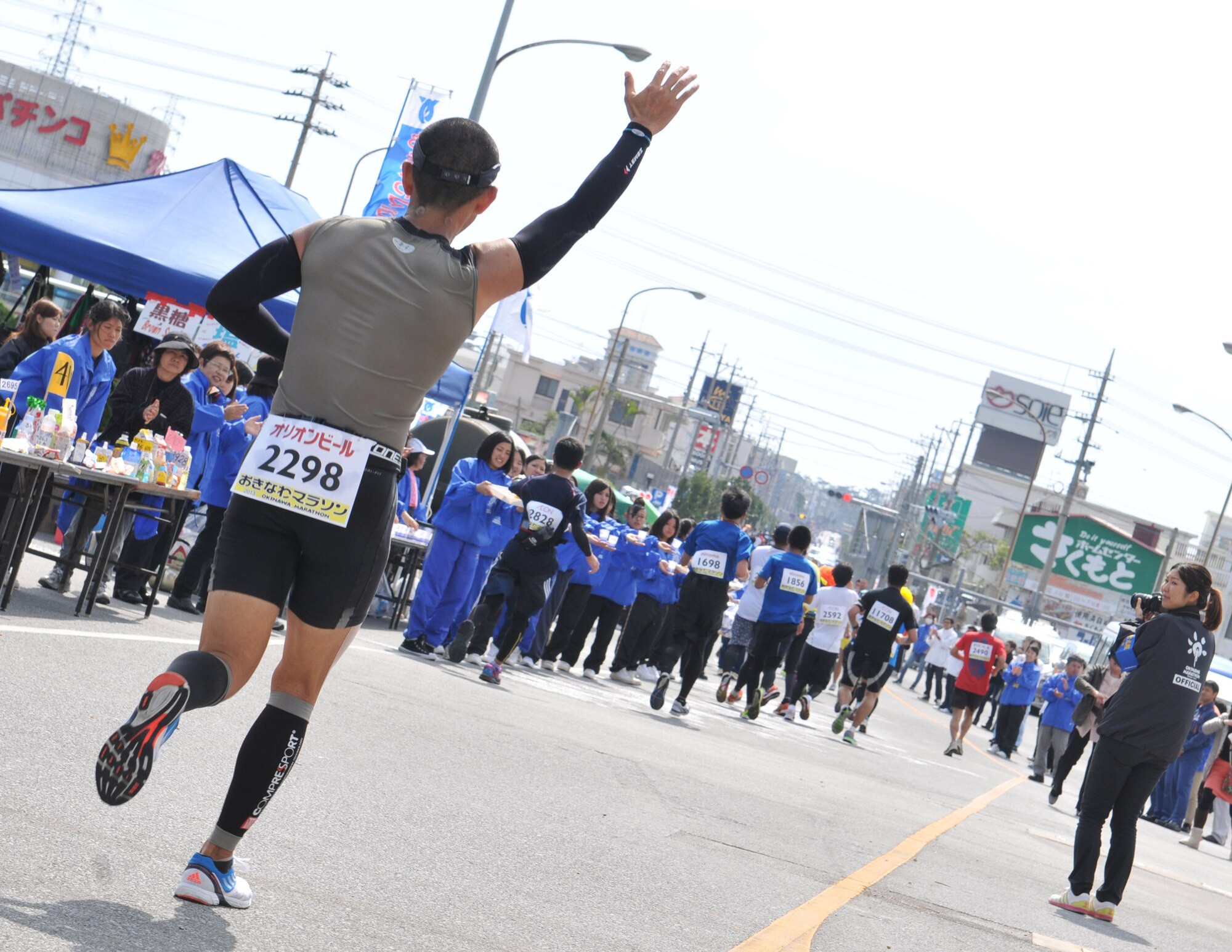 A participant of the 2013 Okinawa Marathon waves goodbye as he exits Kadena Air Base, Japan, Feb. 17, 2013. The 2.8-km portion of the race allowed runners to enter the base from Gate 2 and make their way down past the Kadena Exchange and Kadena High School, exiting out of Gate 5. (U.S. Air Force photo/Airman 1st Class Keith A. James)