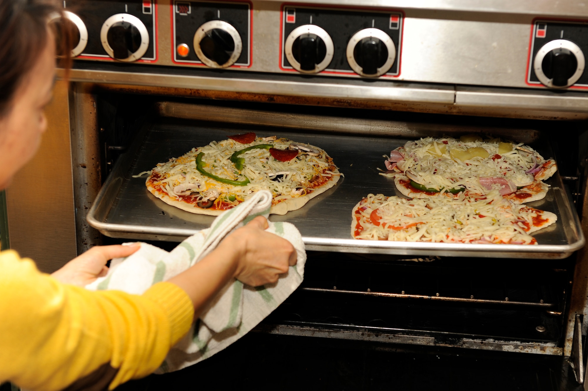 Ms. Komang Goins, 8th Fighter Wing Sonlight Inn director, pulls pizzas out of an oven during a cooking class at Kunsan Air Base, Republic of Korea, Feb. 20, 2013. Kunsan Airmen learned how to make pizza from scratch over their lunch hour. (U.S. Air Force photo by Senior Airman Marcus Morris/Released)