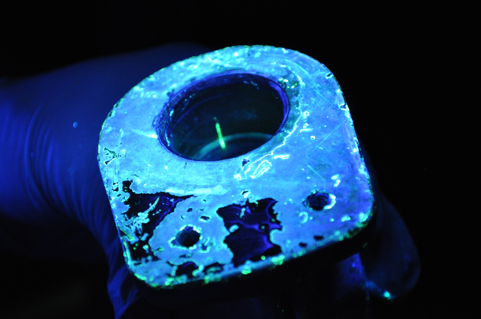 The non-destructive Inspection lab uses a black light during the final step of the penetrant test in order to detect unseen cracks.  The green line in the center of this hydraulic resevoir represents a crack that is not visible to the human eye under normal light.  (U.S. Air Force photo by Senior Airman Mark Hybers)