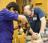Joshua Fabian, Team 4063 electrical team member, drills a hole into a piece of wood for later use on Team 4063’s robot while 2nd Lt. Anthony Pergola, 47th Student Squadron and Team 4063 mentor, helps hold the piece down for safety at the Del Rio High School engineering shop Feb. 14, 2013. For six weeks, the students planned and developed the robot to compete at the ‘Ultimate Ascent’ preliminaries in Lubbock, Texas, Feb. 28 through March 2. (U.S. Air Force photo/Senior Airman Nathan Maysonet)