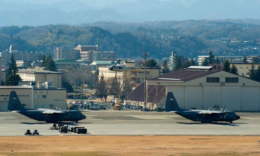YOKOTA AIR BASE, Japan-- Two C-130 Hercules wait to take off as a UH-1N Huey hovers over the aircraft at Yokota Air Base, Japan, Feb. 21, 2013.  The C-130s aircrews demonstrated their airlift capabilities during a readiness week. (U.S. Air Force photo by Airman 1st Class Meagan Schutter)
