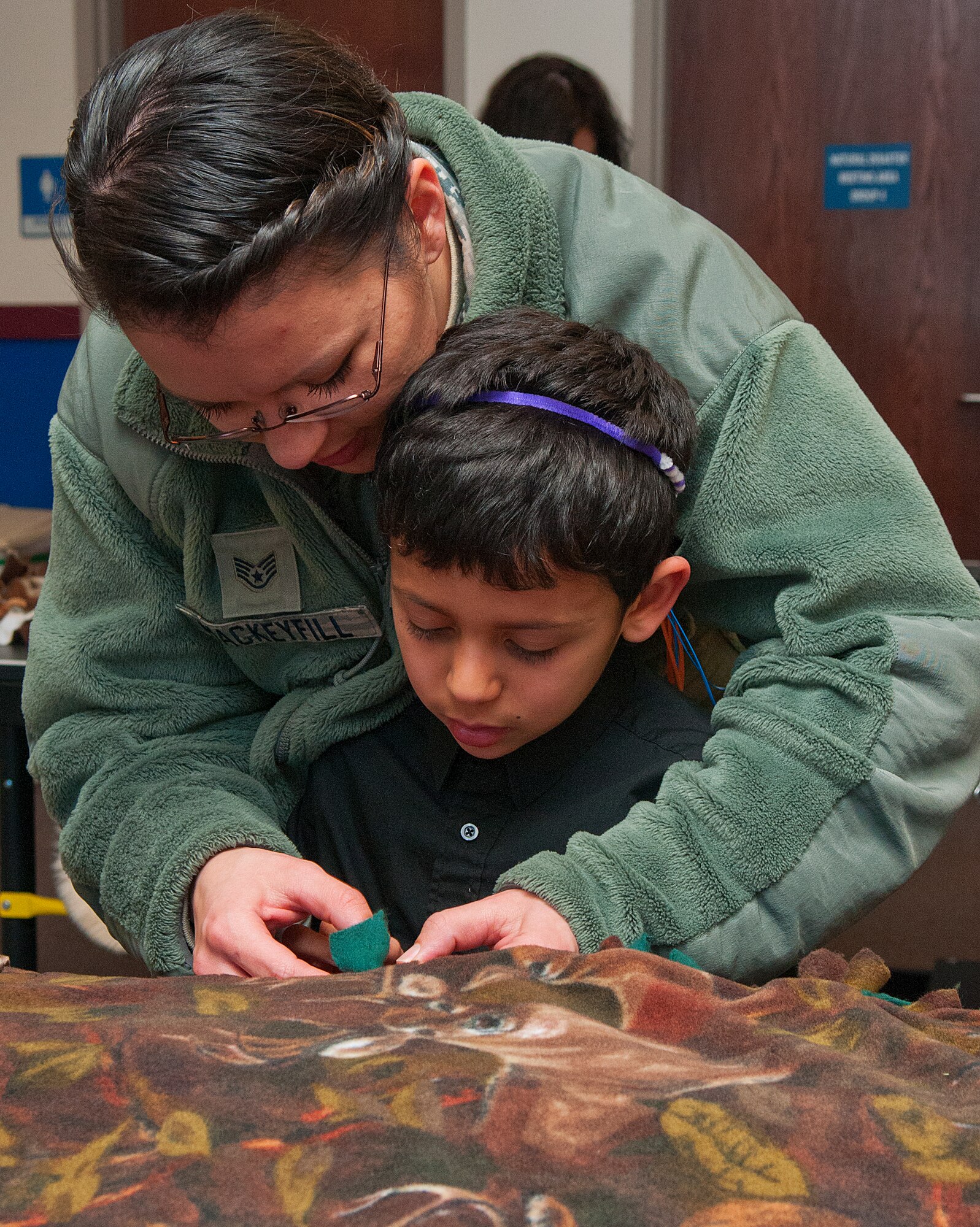 Staff Sgt. Jennifer Mackeyfill, 90th Maintenance Squadron, works with her son, Gabryeal, 7, tie knots around the edge of a lap blanket Feb. 14, at the F. E. Warren Youth Center. The Mackeyfills took part in a community service project, sponsored by the youth center, which made lap blankets to donate to the Cheyenne Veteran Affairs Medical Center’s nursing facility. (U.S. Air Force photo by R.J. Oriez)