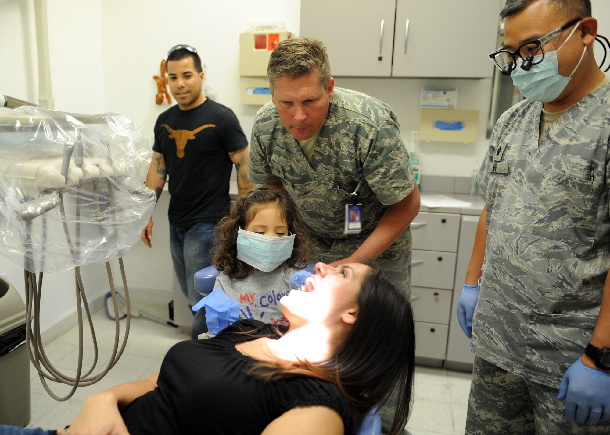 SOUTHWEST ASIA - Blanca prepares to look at her mother’s teeth with the help of Master Sgt. James Bunce, 379th Expeditionary Medical Group dental technician on Feb. 17.  Master Sgt. Jason Olivencia, Air Force Central Command A63 superintendent, and his wife, Katie, brought their daughter to the 379th EMDG Clinic as part of the clinic’s support of National Children’s Dental Health Month. After Blanca was finished playing dentist, she received a dental exam by the dentist, Lt. Col. Son Vu. (U.S. Air Force photo/Senior Airman Joel Mease)