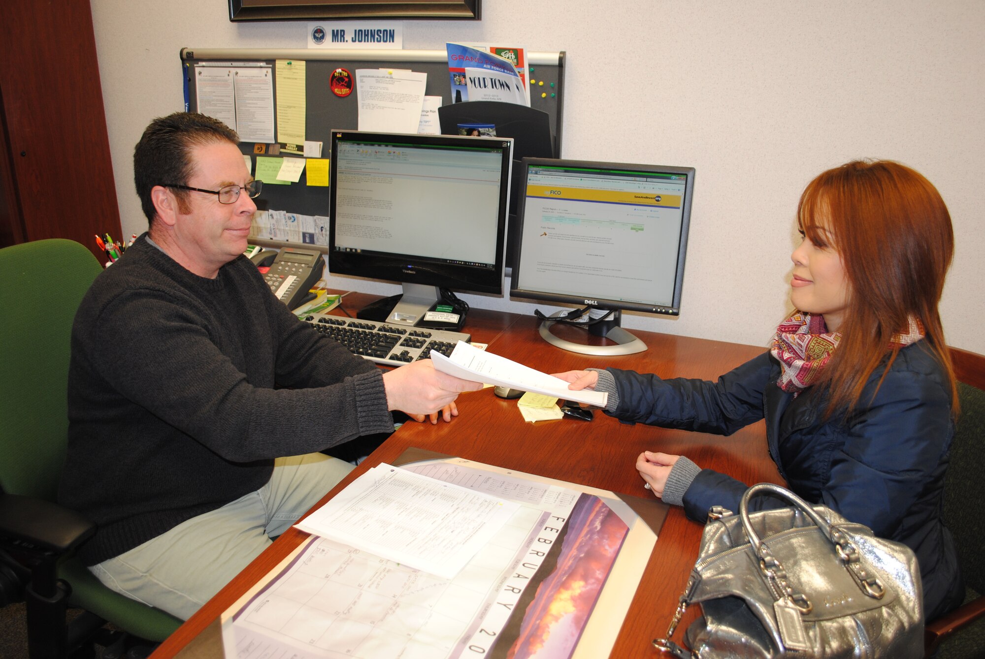Mike Johnson, Airman & Family Readiness Center community readiness consultant, hands Sounthon Loza Gutierrez,Air Force spouse, her credit report on Feb. 21, 2013, on Grand Forks Air Force Base, N.D. Free copies of individual credit reports are being provided to base personnel and their family members on an appointment basis during this year’s Military Saves Week Campaign. (U.S. Air Force photo)