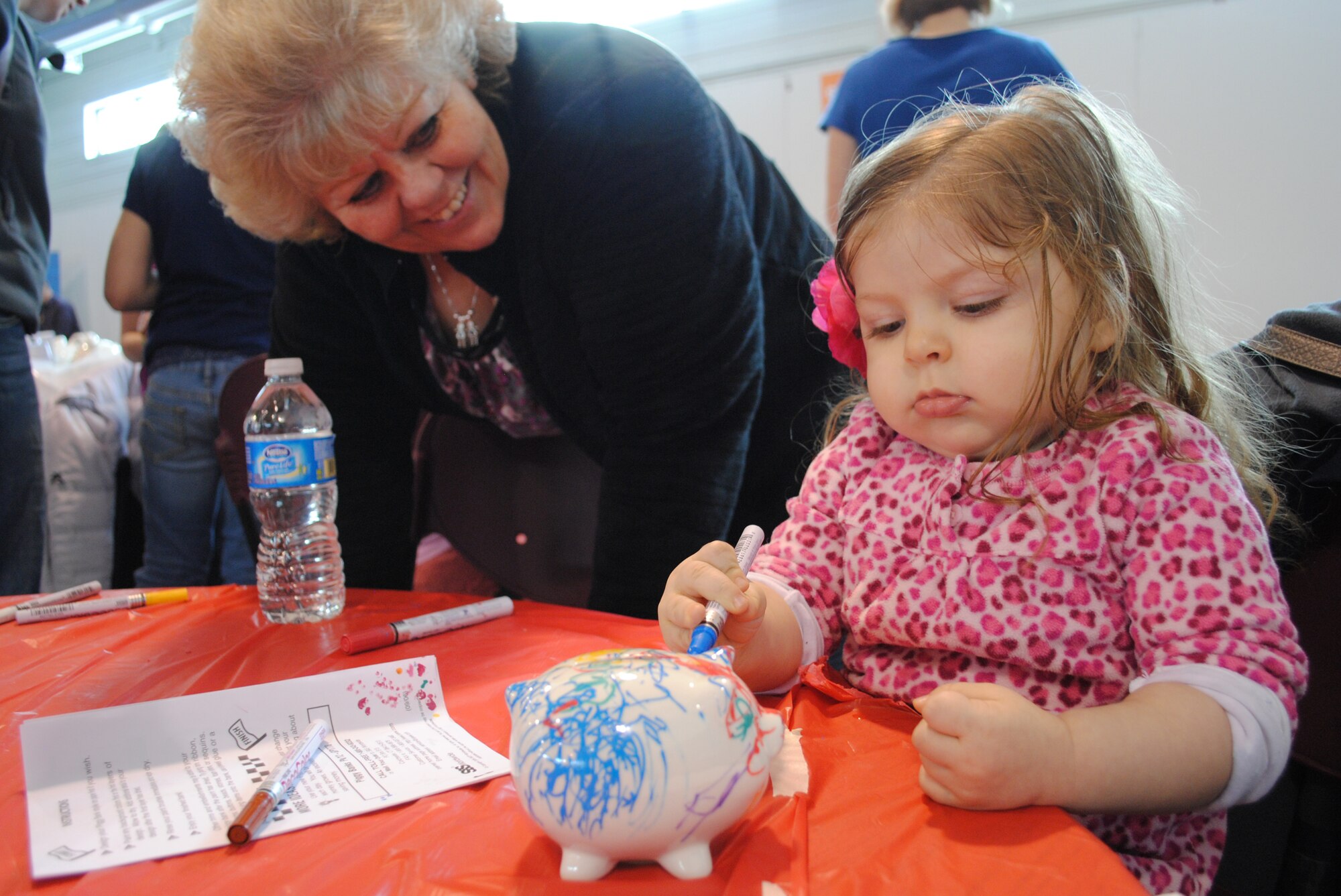 Lillith Carroll, the 23-month-old daughter of Tech. Sgt. Erik Carroll, paints a ceramic piggy bank while her maternal grandmother, Janette Rivera, looks on during a children’s financial on Feb. 21, 2013, at Grand Forks Air Force Base, N.D. (U.S. Air Force photo/Senior Airman Luis Loza Gutierrez)