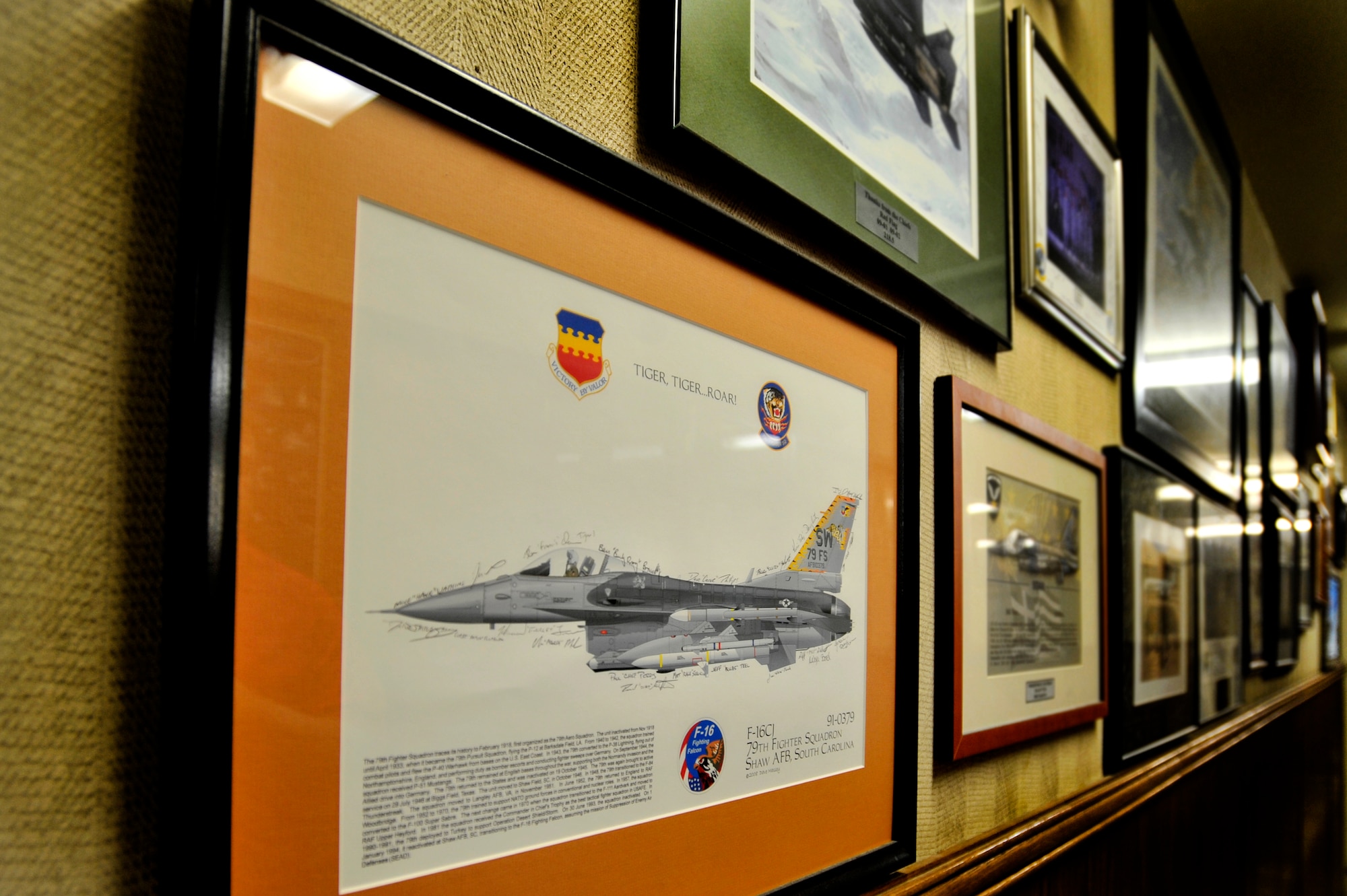 A framed 79th Fighter Squadron image is displayed on the wall of the 414th Combat Training Squadron’s Red Flag building, Feb. 22, 2013, Nellis Air Force Base, Nev. Fred Whitehead, 414th CTS database management, took on the project of organizing and displaying the plaques given to the Red Flag staff by units that have participated in previous Red Flag exercises. Among these mementos are 79th FS plaques dating back to the early 1990s. (U.S. Air Force photo by Staff Sgt. Kenny Holston\Released) 