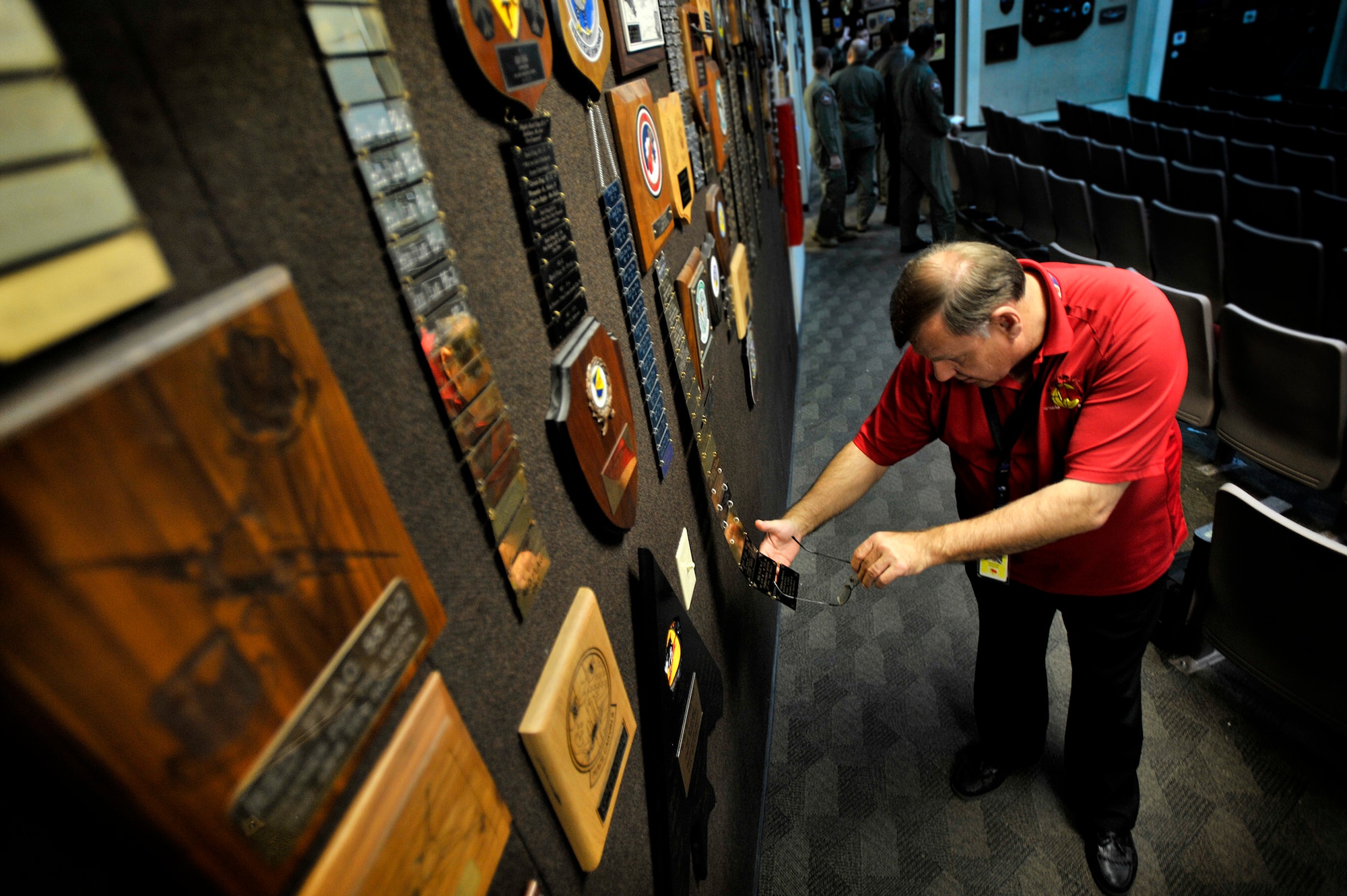 Fred Whitehead, 414th Combat Training Squadron database management explains the history behind the plaques displayed on the wall of the 414th CTS Red Flag auditorium, Feb. 22, 2013, Nellis Air Force Base, Nev. Among these mementos are 79th Fighter Squadron plaques dating back to the early 1990s. Whitehead explained that by displaying the plaques on the auditorium walls, it preserves each units spot in Red Flag history. (U.S. Air Force photo by Staff Sgt. Kenny Holston\Released)