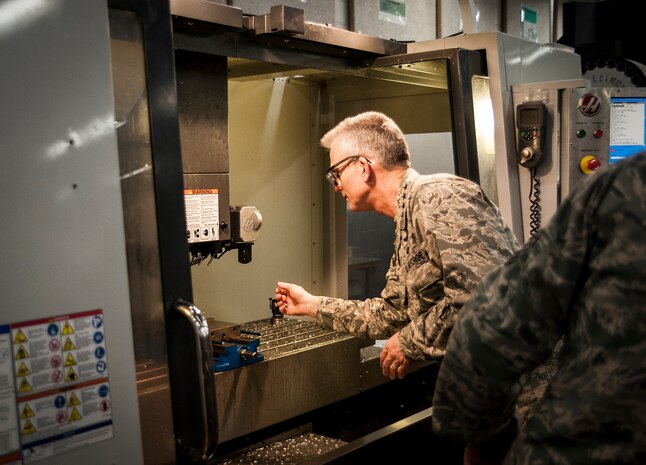 General Paul Selva, Air Mobility Command commander, reaches into a computer operated drill to look at a piece of metal fabricated at the 437th Aircraft Maintenance Squadron Metals Technology shop during a tour Feb. 13, 2013, at Joint Base Charleston – Air Base, S.C. Selva and Chief Master Sgt. Richard Kaiser, AMC command chief, arrived at JB Charleston, Feb. 13, 2013, for a three-day visit of extended tours of AMC units and installations JB Charleston. (U.S. Air Force photo/Senior Airman Dennis Sloan)