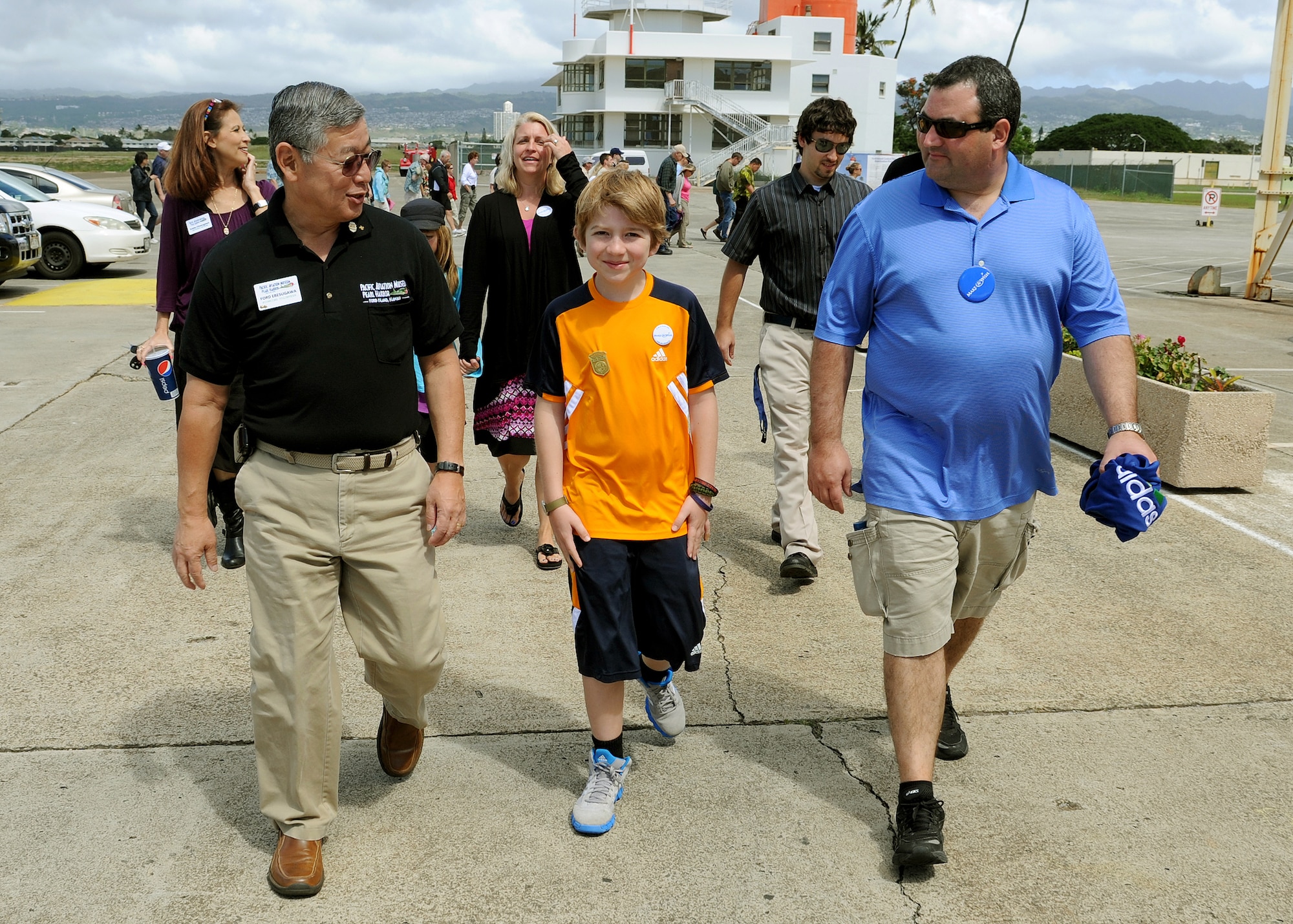Ford Ebesugawa, tour guide (left), Carl Hess, Make-A-Wish recipient (center), and his father James Sullivan (right) walk to Hangar 79 to view various World War II aircraft at the Pacific Aviation Museum, Ford Island, Hawaii, Feb. 19, 2013. Carl is fighting acute lymphoblastic leukemia (ALL), a fast-growing cancer of the white blood cells, and wished to be a downed World War II pilot. During his visit, he received a rare opportunity to spend the night aboard the USS Missouri, fly in a bi-plane, and tour various historical WWII sites. (U.S. Air Force photo/Tech. Sgt. Jerome S. Tayborn)