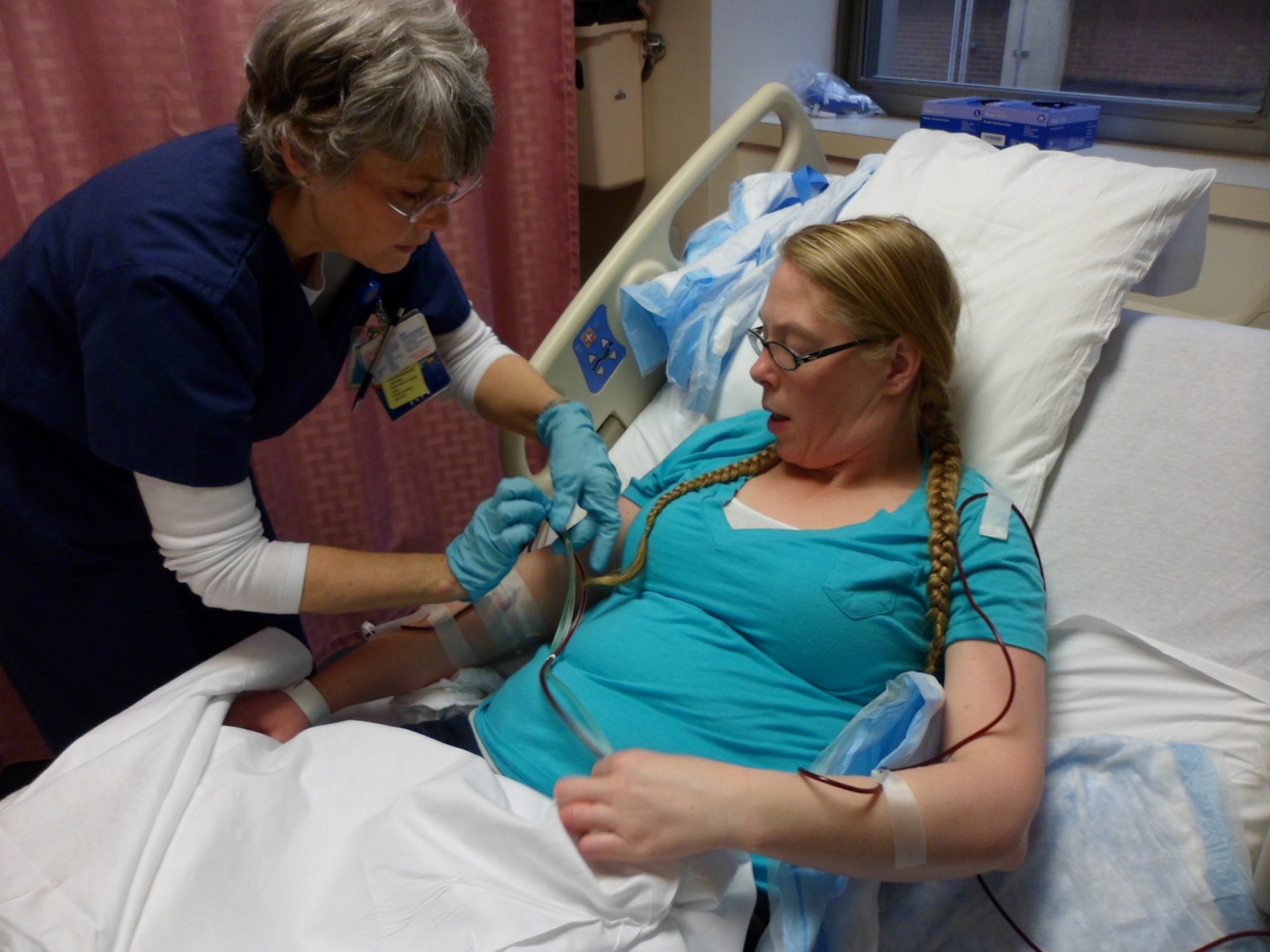 From left, Cindy Solomonda, a registered nurse, tapes tubing from a needle to Tammy Bender’s arm Feb. 19, 2013, during a donation procedure at Georgetown University Hospital in Washington, D.C. Bender, a 100th Communications Squadron spouse, donated bone marrow and blood stem cells thanks to a visit to the The Exchange at RAF Mildenhall in May 2012. After visiting a booth where medical staff were looking for matching donors for a patient at RAF Lakenheath, she received a cheek swab and ended up on the C.W. Bill Young Department of Defense Marrow Donor Program registry. This later resulted in her being a 100 percent match for another patient in the United States. (Courtesy photo by Amanda Stahl)