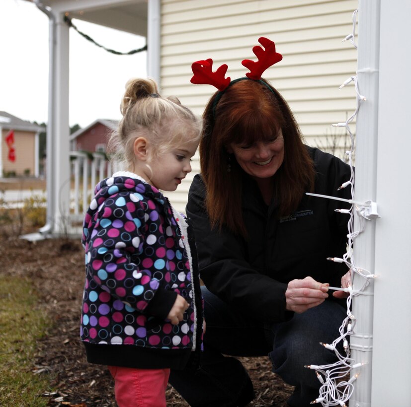 A volunteer from Atlantic Marine Corps Communities housing along with a military child work to put up lights on homes in Berkley Manor for Elf Day aboard Marine Corps Base Camp Lejeune Dec. 7.  Elf Day was established to assist families of deployed service members or those who may just need a little extra assistance from Santa’s helpers during the busy time.