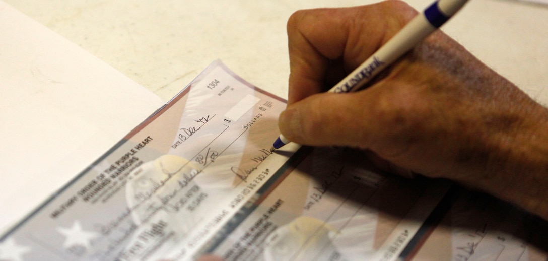 A member of the Military Order of the Purple Heart writes a check for a wounded warrior to supplement his expenses for transportation in Jacksonville, N.C., Dec. 13. MOPH raised approximately $369,000 to donate to service members who were awarded the Purple Heart to be able to receive funds to travel home this holiday season.