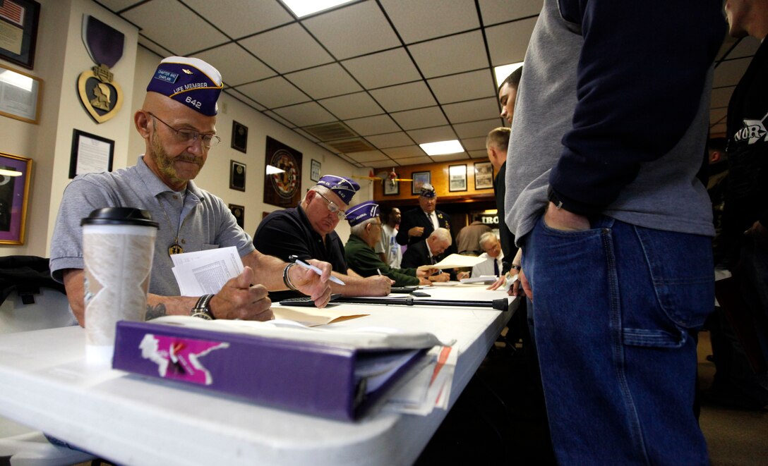 Service members present their military identification cards to show the legitimacy of their Purple Heart award at a check-writing event hosted by the Military Order of the Purple Heart in Jacksonville, N.C., Dec. 13. MOPH raised approximately $369,000 for service members who were awarded the Purple Heart to be able to travel home this holiday season. 