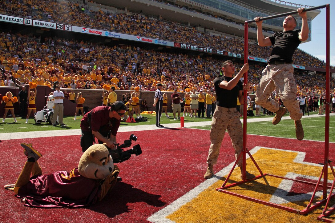 Goldy, University of Minnesota's mascot, watches Lance Cpl. Enrique A. Gutierrez hold the bar for Officer Selection Station Twin Cities' 1st Lt. Andrew Schroers during a pull-up challenge in the endzone at TCF Bank Stadium on Sept. 15. Schroers, 27, from Belle Plaine, Minn., had 30 seconds to complete as many pull-ups as possible. For additional imagery from the event, visit www.facebook.com/rstwincities.