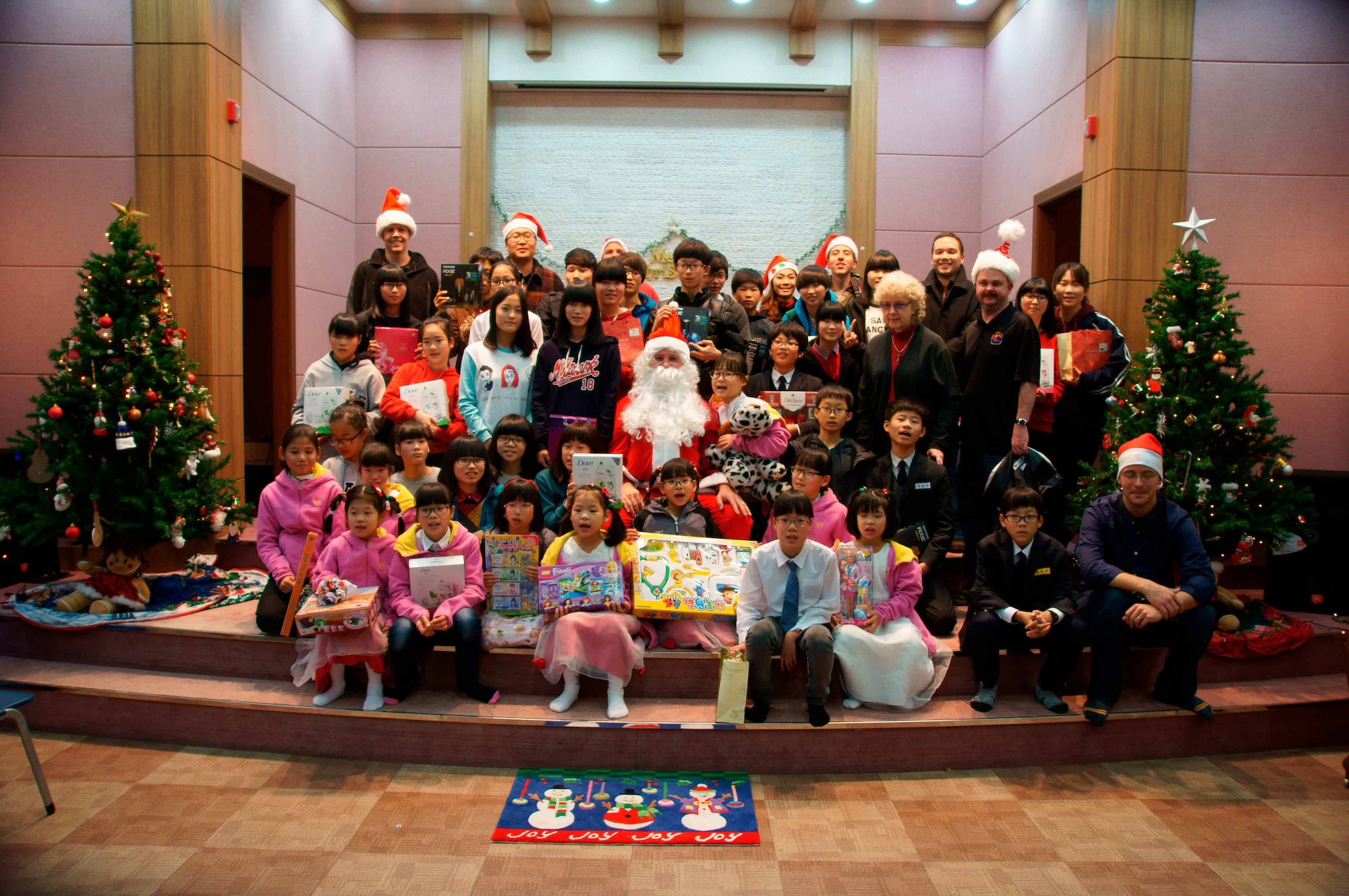 Airmen from the Air Force Technical Applications Center's Detachment 452 pose with Jane White (standing, fourth from right of tree) and kids from the Chechon Children's Home, an orphanage near Wonju, South Korea.  The Airmen visited the facility Dec. 22, 2012 to distribute toys and gifts to the children.   Since 1966, AFTAC has sponsored the local orphanage that has been in operation for nearly 50 years. (Courtesy photo)