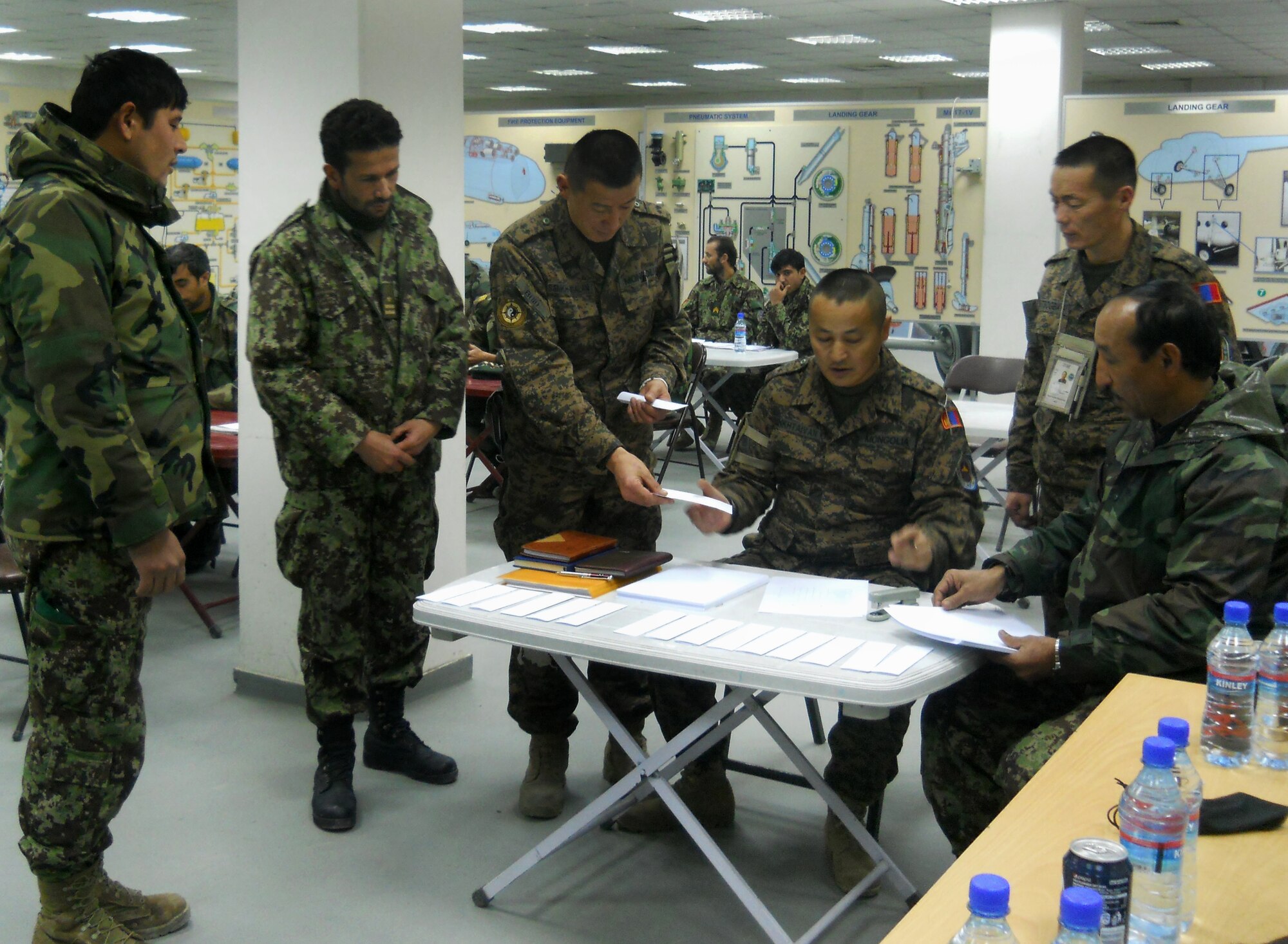 Afghan Air Force maintenance instructors and Mongolian Air Force mentors talk through written test administration during an Mi-17 helicopter ‘Engine & Body’ course at the Kabul, Afghanistan, International Airport, Dec. 17, 2012. Afghan AF Capt. Abdul (second from left) stands aside Mongolian AF Lt. Lt. Enkh-amgalan Sosorbaram (third from left). Abdul was Sosorbaram’s student during Sosorbaram’s first deployment to the NATO Air Training mission. Abdul is now an Mi-17 maintenance instructor as Sosorbaram serves his second deployment advising Mi-17 course development. The Afghan AF’s newest 16 Mi-17 helicopter technicians crossed a stage Dec. 20, 2012 at the airport, receiving certificates from Afghan AF leaders, Mongolian advisors, and 438th Expeditionary Wing leadership. (Courtesy photo)