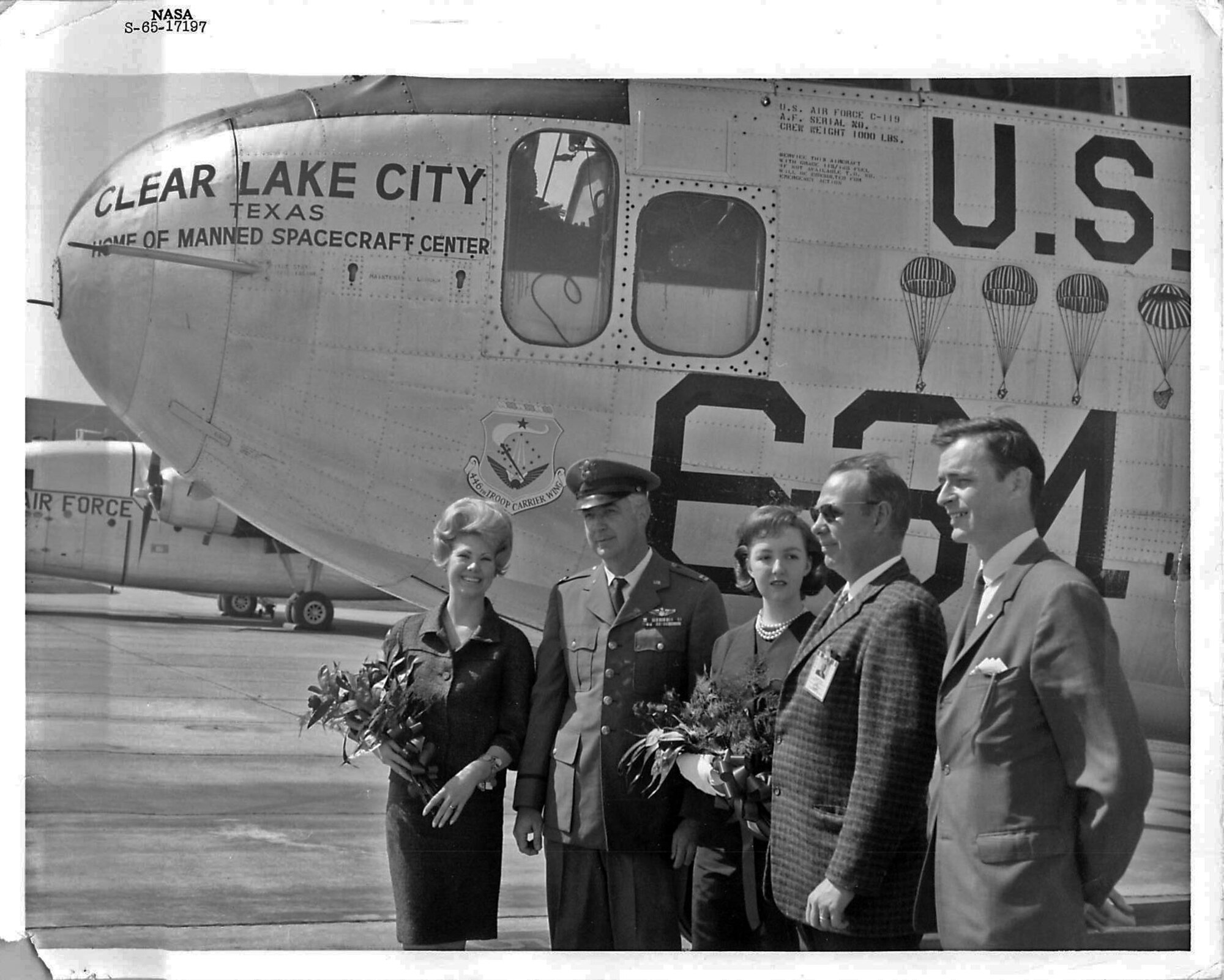 A group of people pose with a C-119J on Ellington Air Force Base, Texas, in 1965. The aircraft was used in support of the NASA Mercury boilermaker capsule program from 1961 to 1967. The emblem behind the woman's head on the left is the original 446th Troop Carrier wing logo. The parachutes on the right side of the photograph indicate the capsule drops that particular aircraft accomplished with NASA. (Courtesy Photo)