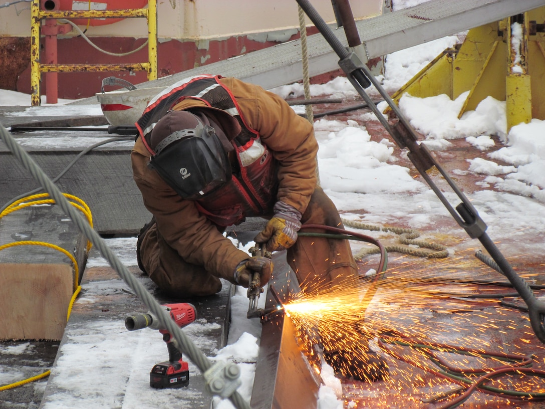 Using a torch, a worker trims a channel brace to be used to hold the Owen M. Frederick tug in place. Four of these channels will be welded to the deck of the barge and hull of the tug.