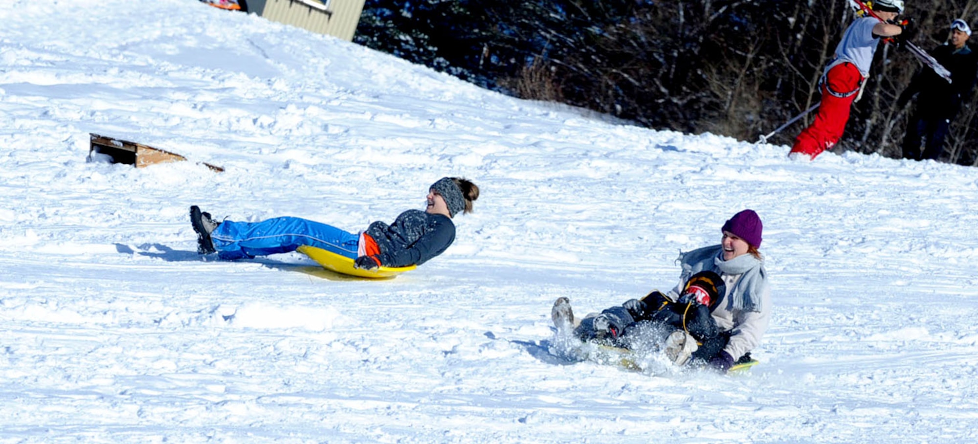 Sledders laugh while going down a hill outside the Land Memorial Ski Lodge at Misawa Air Base, Japan, Jan. 5, 2013. To maximize “family fun” time, on Saturdays and Sundays, from 10:30 a.m. to 3 p.m., orders can be called into the Lakeview Grille and delivered to the lodge. In just a few moments, families can enjoy delicious cracker-crust pizza and fresh donuts in a warm cabin overlooking the snow. Customers can also bring their own food, drinks and, if not in bottles, beer. (U.S. Air Force photo by Airman 1st Class Kenna Jackson)