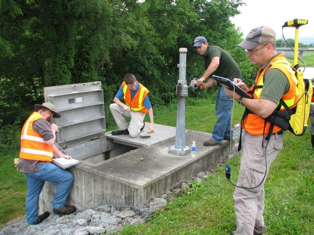 A Baltimore District team of engineers takes detailed notes as Lucas Gagnon, Town of Moorefield, W. Va., director of public works, raises and lowers a sluice gate during the periodic inspection on the Moorefield South flood risk management system.  Dan Risley (right) inputs data on a Corps-developed geographic information system to pinpoint inspection data.
