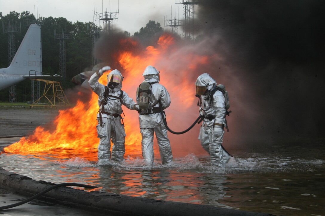 Marines with air station Aircraft Rescue and Firefighting works on putting out a fire in a pit of water and jet fuel during a fuel fire training.