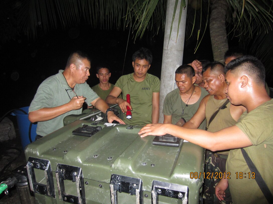 Frank Duran, the U.S. Marine Corps Forces, Pacific Experimentation Center water purification project lead, uses flashlights to provide training on the Aspen 2000 water purification system here Dec. 8, in order to provide relief to devastated areas struck by Typhoon Bopha and meet U.S. Pacific Command Science and Technology Program requirements. The MEC was able to gather operational feedback on the water purification systems while providing much-needed water to local communities in the Philippines.
