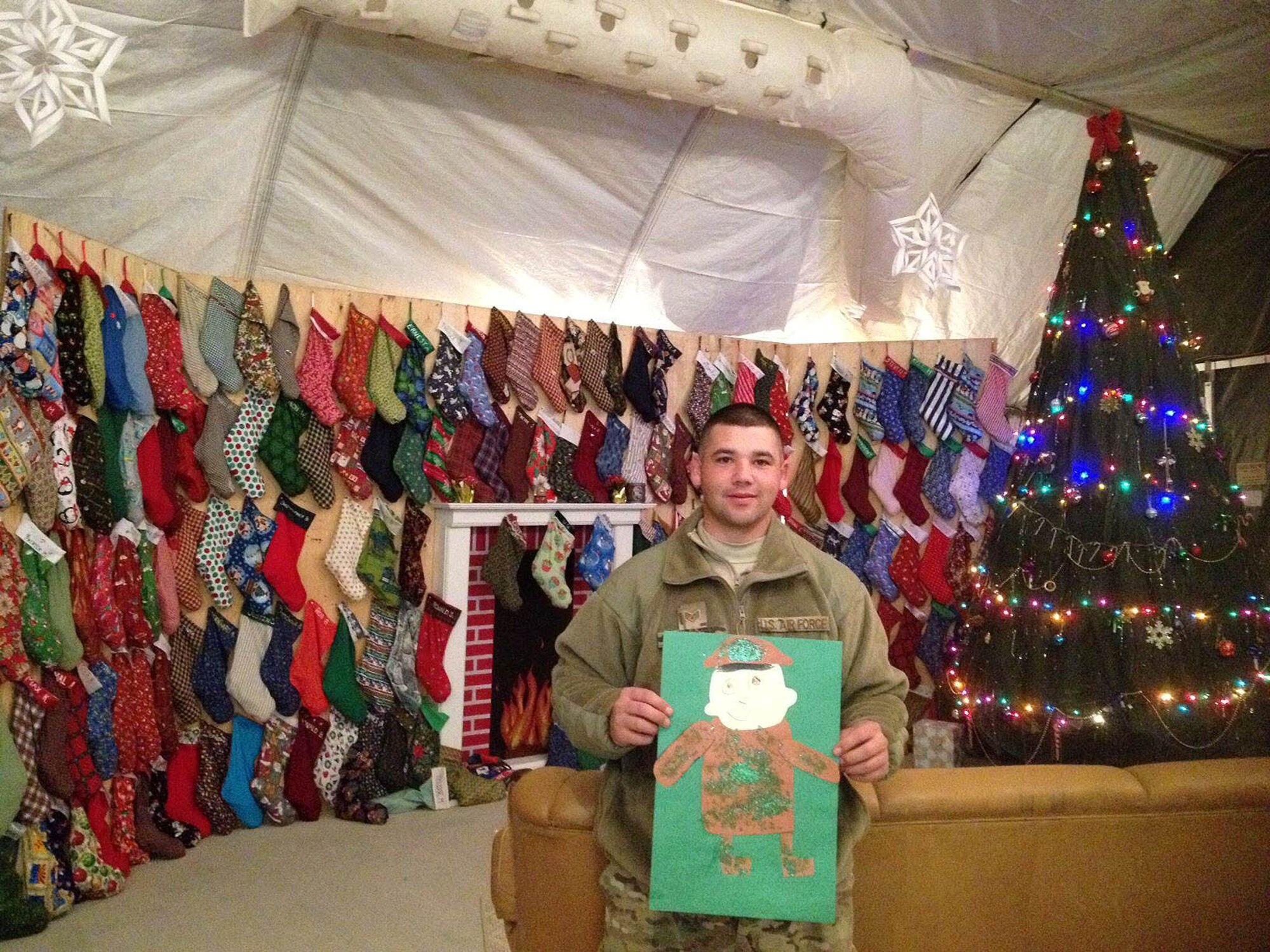 Staff Sgt. David Ramirez, 554th RED HORSE Squadron services technician, hold’s his son’s Christmas card, Dec. 26, 2012, in front of a Christmas scene the Airmen have created while on deployment within the U.S. Central Command area of operations. The cards were sent to Sergeant Ramirez and fellow Airmen from students of the Andersen Elementary School. (Air Force courtesy photo)