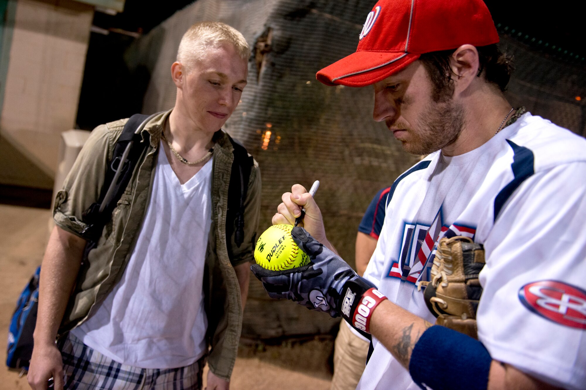 Nick Clark, Wounded Warrior Amputee Softball Team, signs an autograph for Airman Basic Ken Oliver, 15th Maintenance Squadron, Jan. 8, 2013, at Milican Field, Joint Base Pearl Harbor-Hickam, Hawaii. Oliver was one of two Airmen selected to throw out the ceremonial first pitch. The WWAST is comprised of competitive, athletic veterans and active duty servicemembers who have lost limbs during post-9/11 combat operations. The team includes individuals with a variety of amputations of the arm, above knee, below knee, bilateral below knee, and foot. Some are still in the service, while others are attending college thanks to the Post-9/11 GI Bill while others have moved on to new careers. (U.S. Air Force photo/Staff Sgt. Mike Meares)