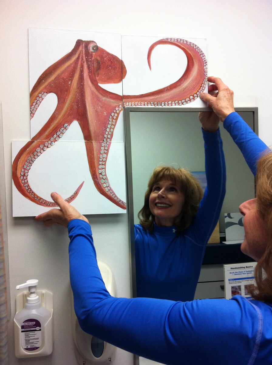 Ildiko Andrews, mother of Capt. Kristine Andrews, 87th Medical Group pediatrician, hangs an octopus painting around a mirror in one of the six pediatric waiting rooms at the clinic Dec. 28, 2012. She, along with seven of her friends from Lake Martin, Ala., who take an art class together, painted and donated approximately 140 paintings for the clinic. (U.S. Air Force photo by Capt. Kristine Andrews/Released)