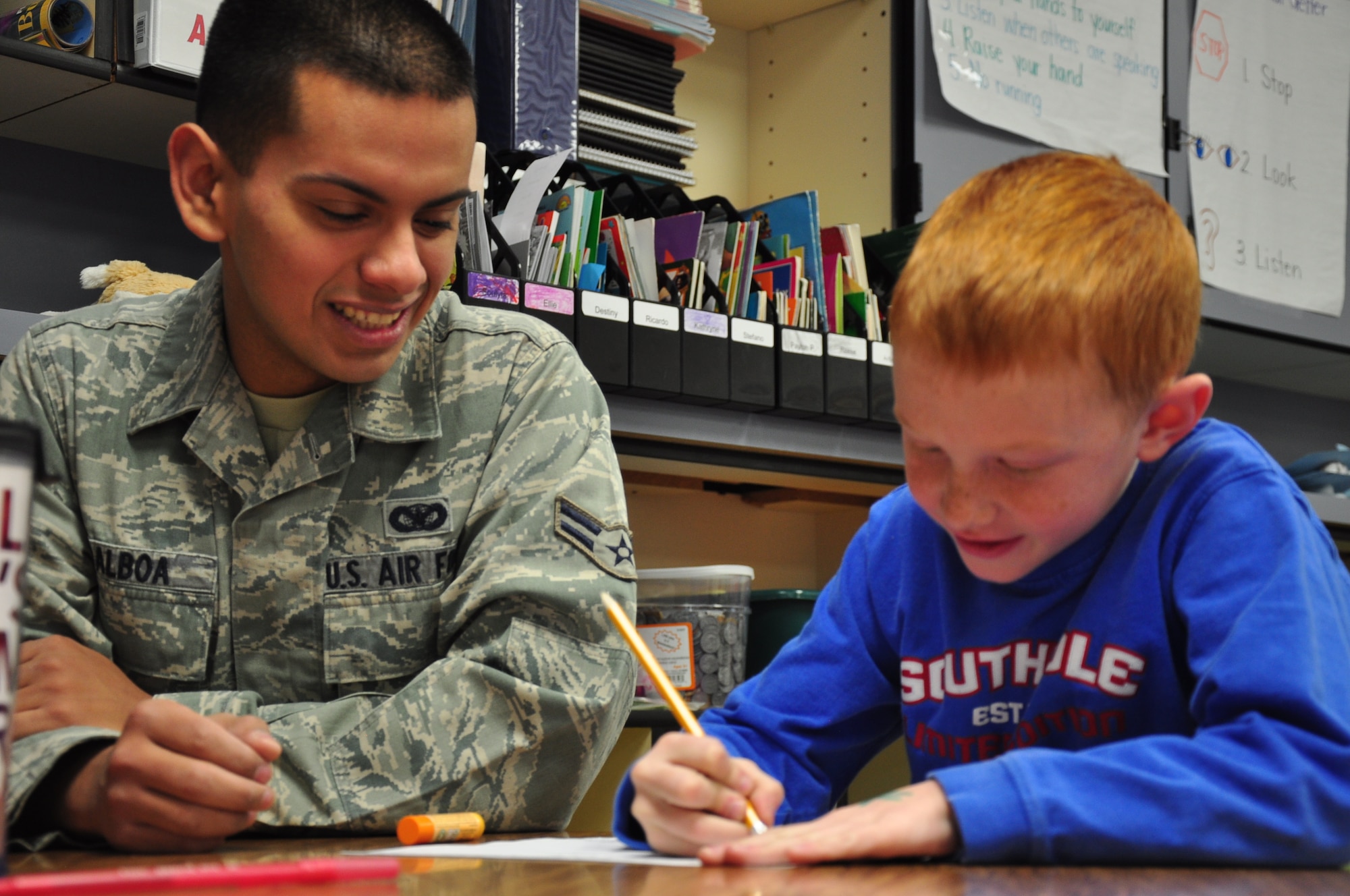 Airman 1st Class Victor Balboa, 90th Missile Security Forces Squadron response force leader, talks with Reese Allen, first grader at Pioneer Park Elementary School, Cheyenne, Wyo., about Allen’s writing assignment Dec. 13. Balboa and other members of the 90th MSFS volunteer regularly at Pioneer Park Elementary, helping children with writing, math and reading skills. (U.S. Air Force photo by Senior Airman Mike Tryon)
