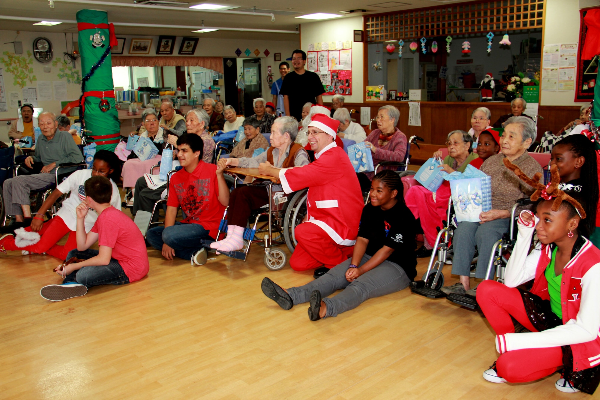 Tech. Sgt. Brian Dieckmann (as Santa), 18th Equipment Maintenance Squadron, Youth Center volunteers and the residents of Ichijoen Elder’s Home, listen to an Ichijoen staff member as they explain the tradition of Okinawan Eisa dancing on Okinawa, Japan, Dec. 22, 2012. Detachment 1, 554th RED HORSE Squadron has been partnering with Ichijoen from July to December after the Erwin Professional Military Education Center’s Class 12-5 hosted a volunteer project at Ichijoen. Two members from Det. 1 continued their relationship with the elder’s home. The squadron visits the home once a month to perform grounds work around the facility, interact with the residents, and provide donations when needed. Det. 1 recently partnered with the Youth Center and coordinated a holiday celebration with the residents, in which they performed Christmas songs for the residents. "The elders were happy to see the Youth Center children sing Christmas songs and dance,” said Yoko Sakiyama, the director of Ichijoen Elder’s Home. The squadron donated tissues, hand towels and lotion to the home. “I was impressed to hear about the volunteer spirit that Americans have. We thank the Youth Center and RED HORSE volunteers for visiting our elders during this busy holiday season." (U.S. Air Force photo/Tech. Sgt. Brian Dieckmann)