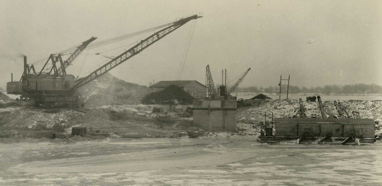 A crane and drag line, which is attached to a dredging bucket, is at work in a sump area of the Livingstone Channel. On the right side of this photo, taken in 1933, is a scow where dredged materials were placed and then pumped to the opposite side of the coffer dam.