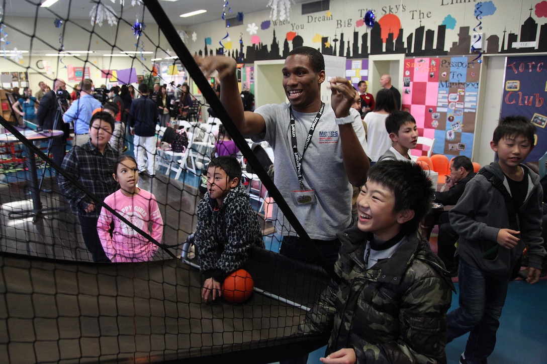 Yoshihito Sakurada watches and smiles while Columbus Wilson III scores a basket Jan. 11 at the Camp Foster Youth Center. Sakurada along with 23 other students from Oshima elementary and middle schools are visiting Okinawa as part of a four-day youth cultural exchange and homestay program. Throughout the children’s stay, they will participate in various events such as arts and crafts, playing games, a Sunday brunch, and visiting an American school before leaving on Jan. 14. Sakurada is an 11-year-old fifth-grade student from Oshima, and Wilson is a program assistant at the Camp Foster Youth Center. (U.S. Marine Corps photo by /Released)