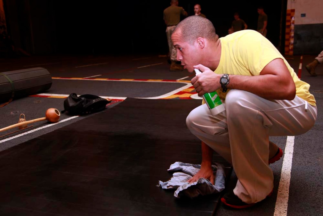 Aviation support equipment technician 2nd Class Juan A. Diaz, , USS Peleliu, cleans off a training mat before conducting a class on Capoeira in the ship's hangar bay, Dec. 6. Capoeira is a form of dancing and martial arts, and the classes are taught to give Marines and sailors a way to decompress in their off-time. The 15th MEU is deployed as part of the Peleliu Amphibious Ready Group as a U.S. Central Command theater reserve force, providing support for maritime security operations and theater security cooperation efforts in the U.S. 5th Fleet area of responsibility. Diaz, 28, is from Bronx, N.Y. (U.S. Marine Corps photo by Cpl. John Robbart III)