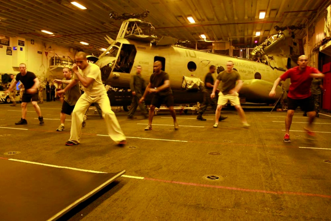 Aviation support equipment technician 2nd Class Juan A. Diaz, USS Peleliu, leads warm-up exercises before a Capoeira class in the ship's hangar bay, Dec. 6. Capoeira is a form of dancing and martial arts, and the classes are taught to give Marines and sailors a way to decompress in their off-time. The 15th MEU is deployed as part of the Peleliu Amphibious Ready Group as a U.S. Central Command theater reserve force, providing support for maritime security operations and theater security cooperation efforts in the U.S. 5th Fleet area of responsibility. Diaz, 28, is from Bronx, N.Y. (U.S. Marine Corps photo by Cpl. John Robbart III)