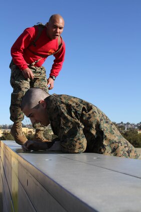 Sgt. Jason A. Sabater, drill instructor, Company C, 1st Recruit Training Battalion, instructors a recruit to climb over a wall during the obstacle course aboard Marine Corps Recruit Depot San Diego Jan. 3. The o-course allows recruits to maneuver through obstacles while building upper-body strength.