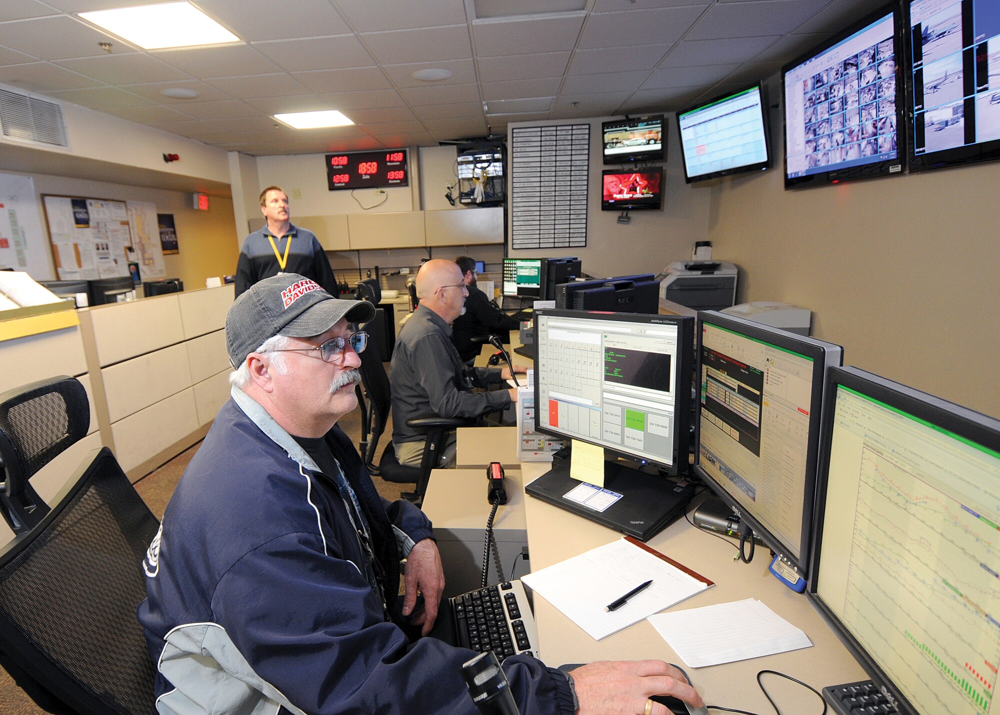 Air Force photo by Margo Wright
If it affects depot operations, it’s known to the production controllers working in the Maintenance Operations Center in Bldg. 3001.  A 24-hour operation that doesn’t take holidays or yield its mission to weather-related base closures, personnel keep constant watch over everything from weather,  emergencies, movement on the flight line and security of buildings.  MOC chief Keith Woolverton, walking, watches a bank of screens while controllers Jim Greiner, Casey Wheeler and Jason Charvoz, from front, keep up with the ever-changing information.