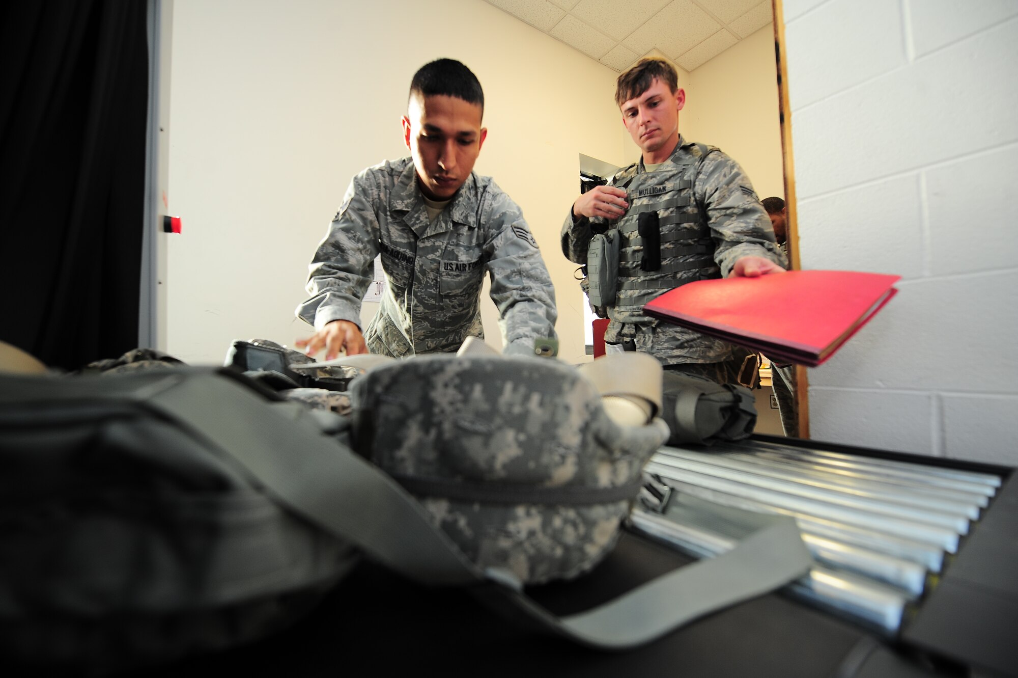 U.S. Air Force Senior Airman Jonathan Garcia-Aquino, 4th Civil Engineer Squadron structures journeyman, and Senior Airman Anthony Mulligan, 4th CES water and fuels systems maintenance journeyman, place gear on a conveyer belt during Operational Readiness Exercise Coronet Warrior 13-01 on Seymour Johnson Air Force Base, N.C., Jan. 14, 2013. The items were sent through an X-ray machine in order to ensure no contraband entered the facility. (U.S. Air Force photo/Airman 1st Class Aubrey White/Released)