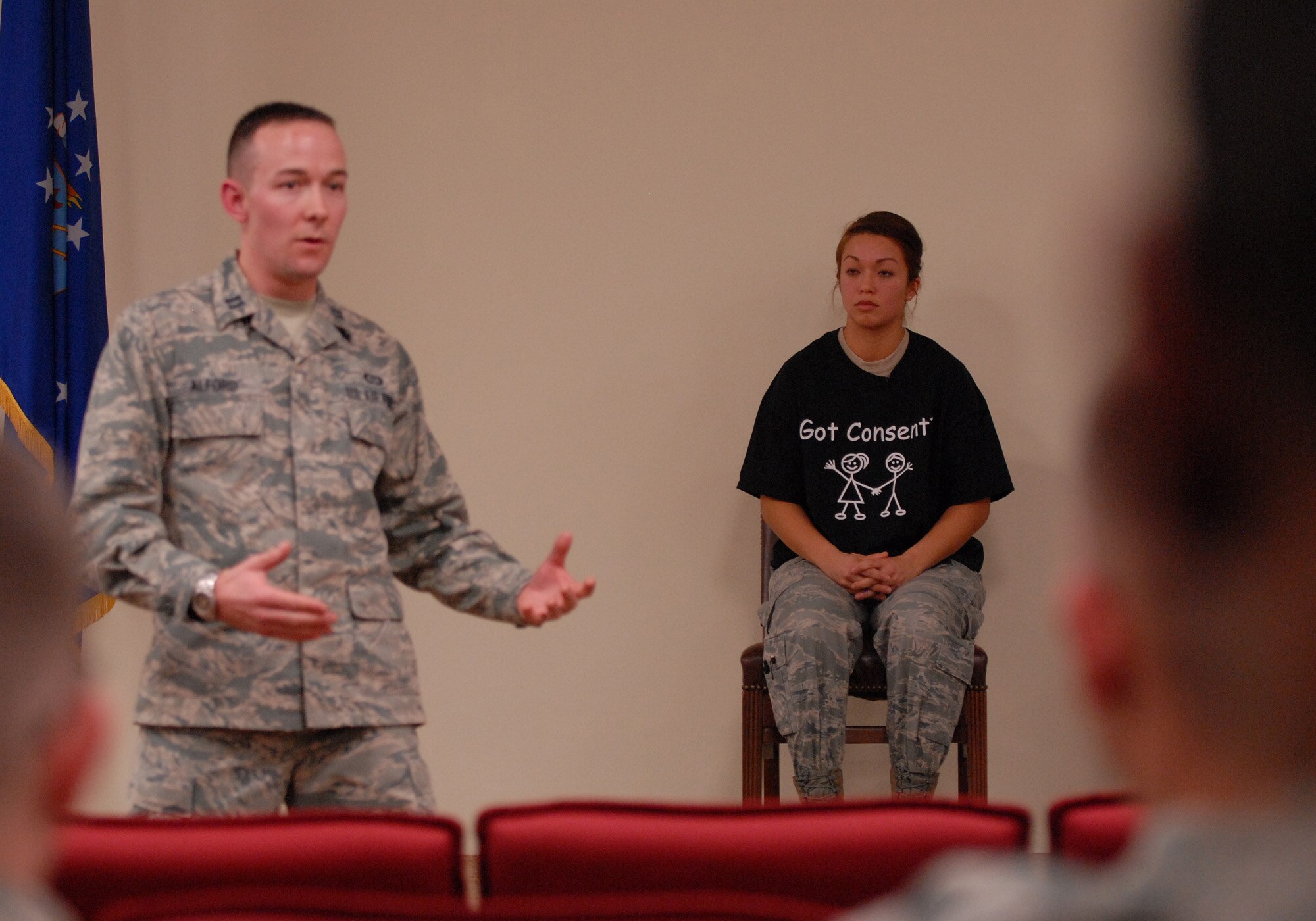 Staff Sgt. Angela  Hicks, sexual assault theater group actress, listens as Capt. Brandon Alford, 8th Fighter Wing assistant sexual assault response coordinator, addresses audience members Dec. 19, 2012, at Kunsan Air Base, Republic of Korea. The goal of the theater group was to address sexual assault issues and possible intervention solutions. (U.S. Air Force photo by Staff Sgt. Tong Duong/Released)