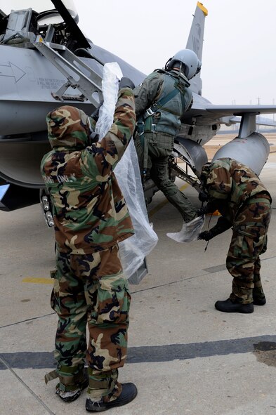 Senior Airman Clinton Caruolo, right, 8th Aircraft Maintenance Squadron, places plastic boots on Lt. Col. Jeremy Quatacker, 8th Fighter Wing chief of safety, as Senior Airman Jonathan Tiley, 8th AMXS, prepares a plastic bag to cover him from hazardous chemicals  during Exercise Beverly Midnight 13-1 at Kunsan Air Base, Republic of Korea, Jan. 16, 2013. The exercise scenario demonstrated the Airmen’s capabilities to accomplish their mission in a contaminated environment. (U.S. Air Force photo by Senior Airman Marcus Morris/Released)