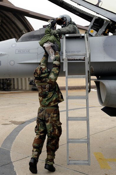 Lt. Col. Jeremy Quatacker, 8th Fighter Wing chief of safety, gives Senior Airman Clinton Caruolo, 8th Aircraft Maintenance Squadron, his bags before exiting an F-16 Fighting Falcon during exercise Beverly Midnight 13-1 at Kunsan Air Base, Republic of Korea, Jan. 16, 2013. The clear bags are  used to keep the pilot free of contaminants before he steps onto the ground. (U.S. Air Force photo by Senior Airman Marcus Morris/Released)