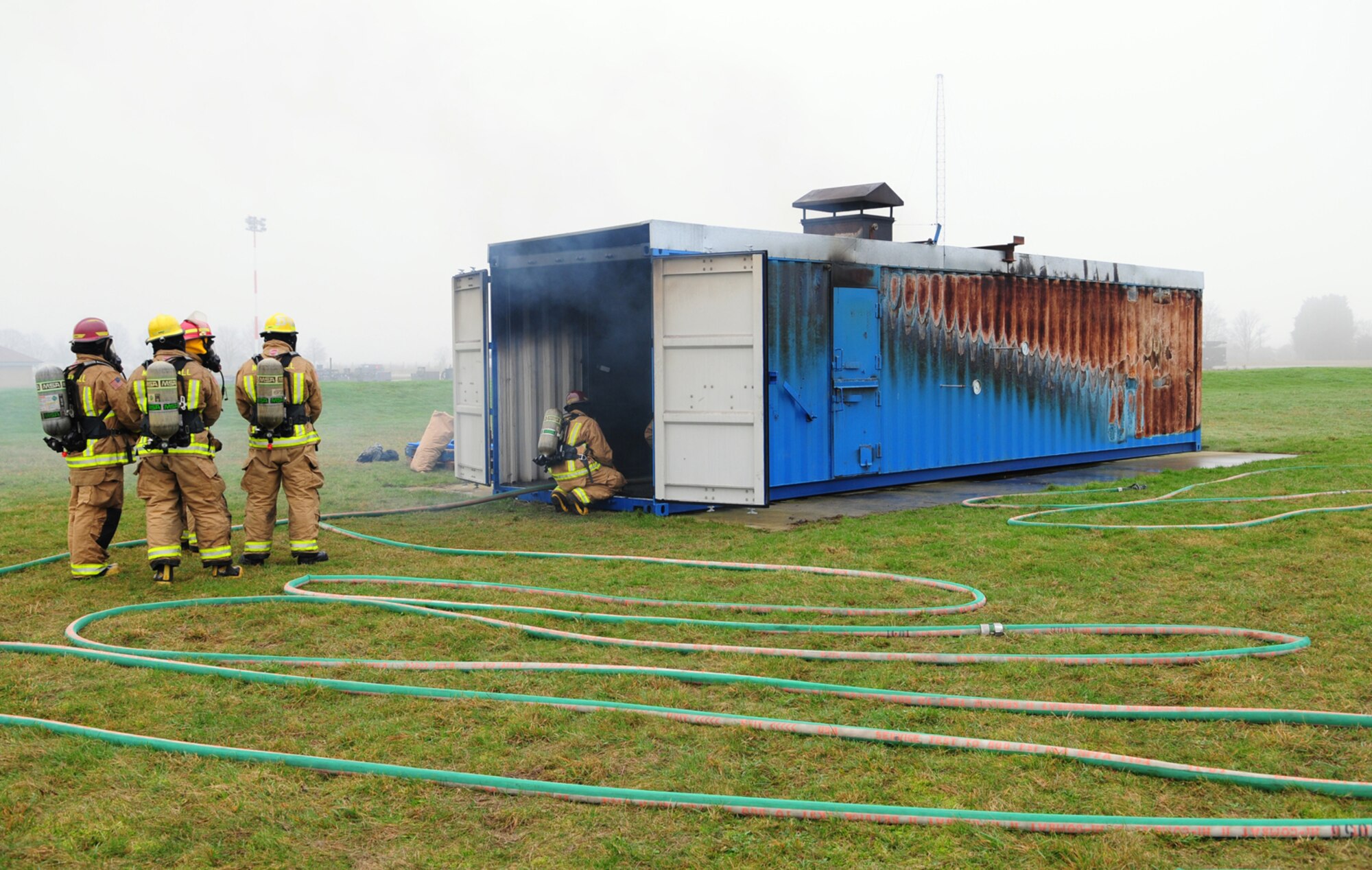 Firefighters wait outside the compartment fire behavior trainer as they prepare to go inside and tackle the fire Jan. 10, 2013, at RAF Mildenhall, England. The fire trainer is a vital aid and allows the firefighters to identify conditions that create flashovers and backdrafts so they can safely attack the fire. (U.S. Air Force photo by Karen Abeyasekere/Released)
