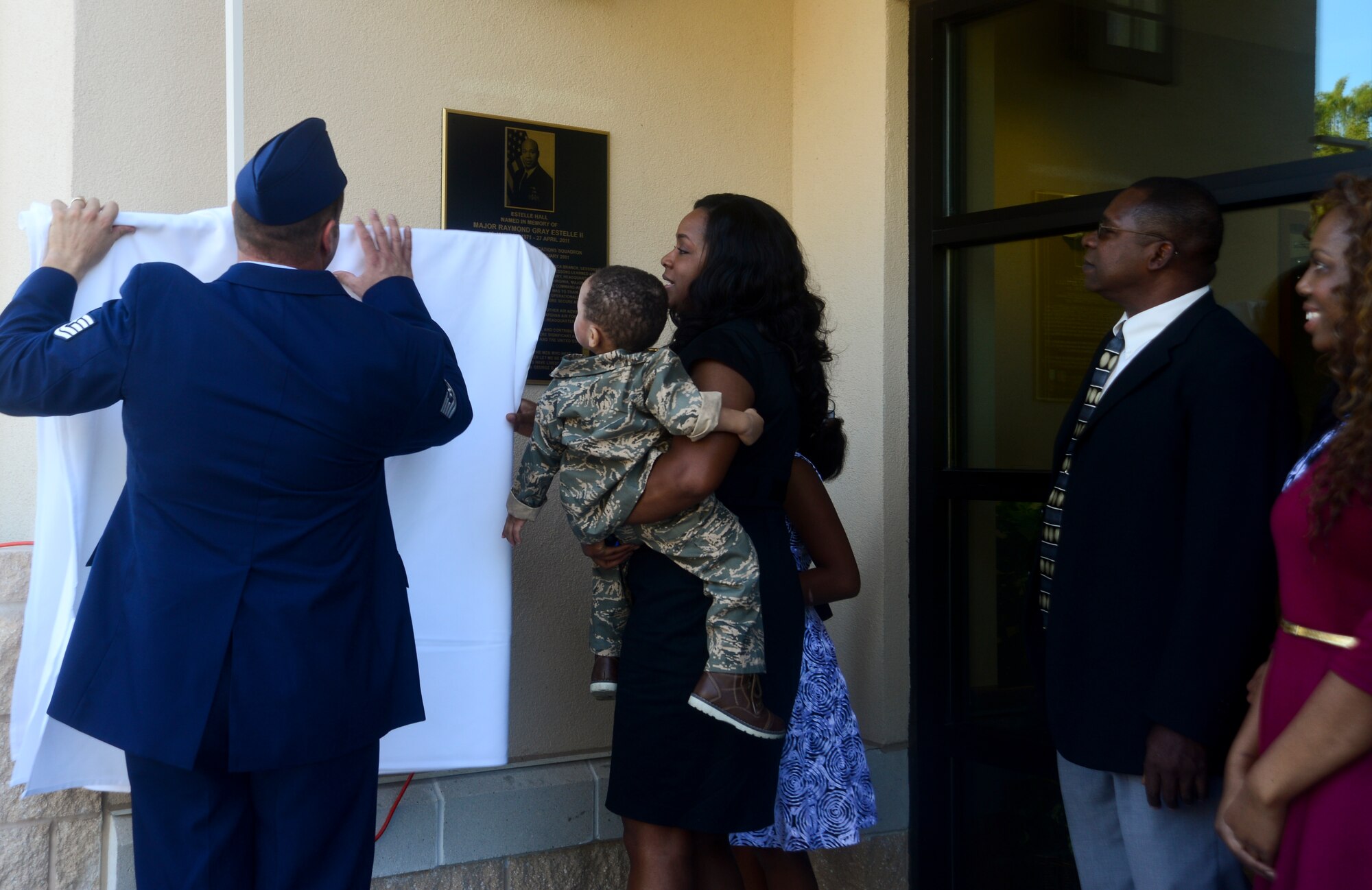 The Estelle family, along with a member of the 6th Communication Squadron, removes the cover over a plaque honoring Maj. Raymond Estelle II at MacDill Air Force Base Fla., Jan. 16, 2013. Estelle was one of nine people killed in action April 27, 2011 and served at MacDill AFB from 1999-2001. (U.S. Air Force photo by Senior Airman Melissa Paradise/Released)